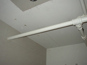 A ceiling with a white pipe hanging from the side of it.