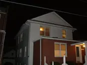 A house with a fence and lights on at night.